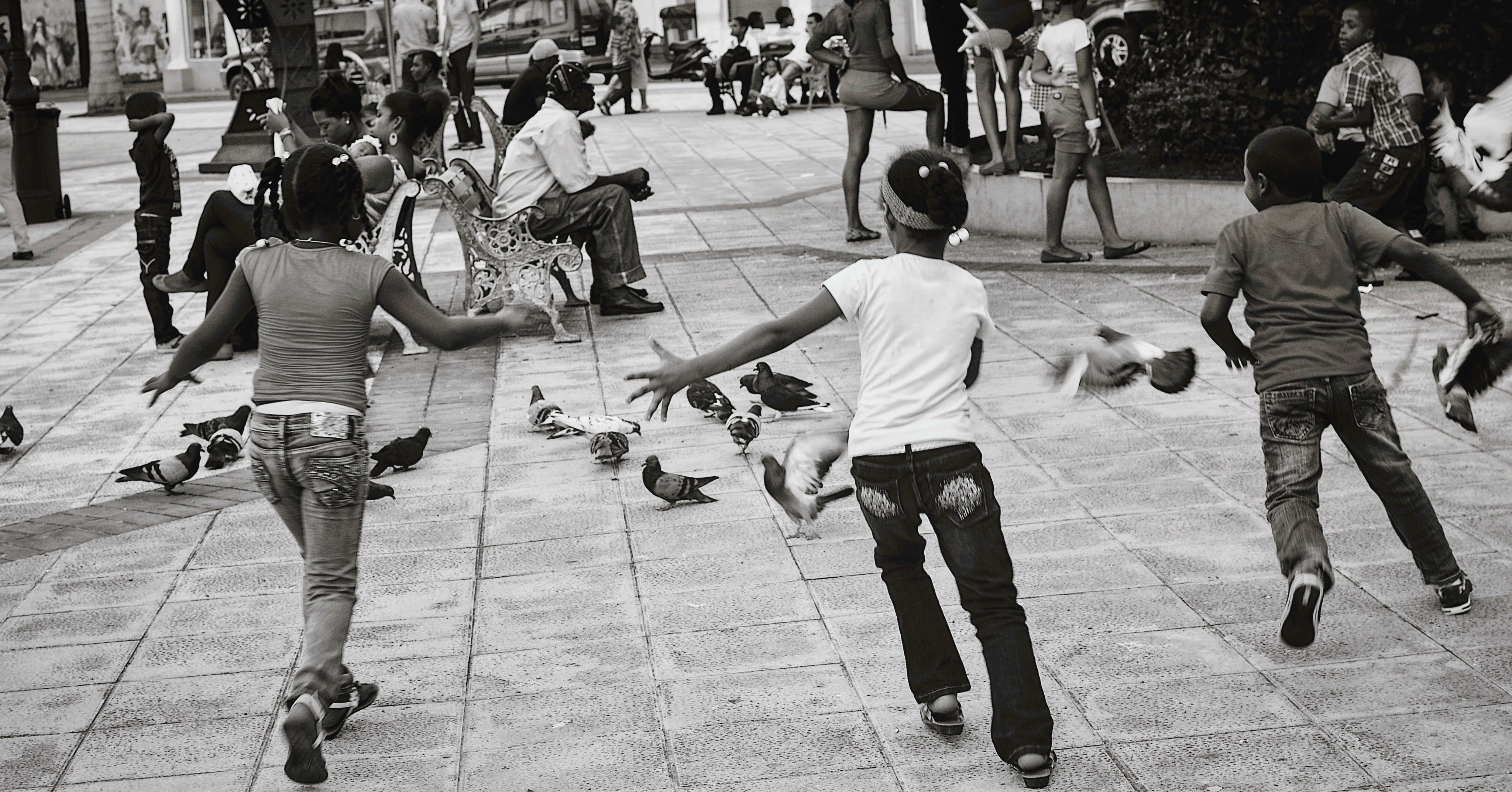 Three Black children playfully chasing birds down the street.